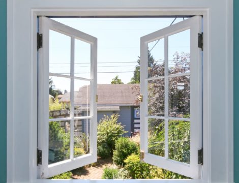 Geöffnetes Fenster mit weißem Rahmen, zum grünen Garten mit kleiner Hütte.